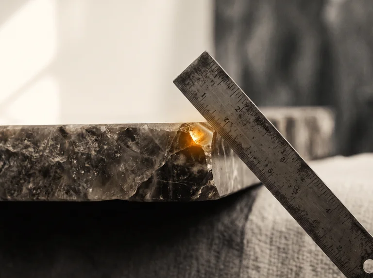 Macro close-up of a polished stone countertop edge with a carpenter's square resting against it at an angle.